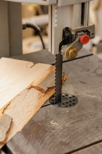 Sierra de cinta vertical que corta tablas de madera en bruto sobre una mesa de trabajo en un taller de carpintería