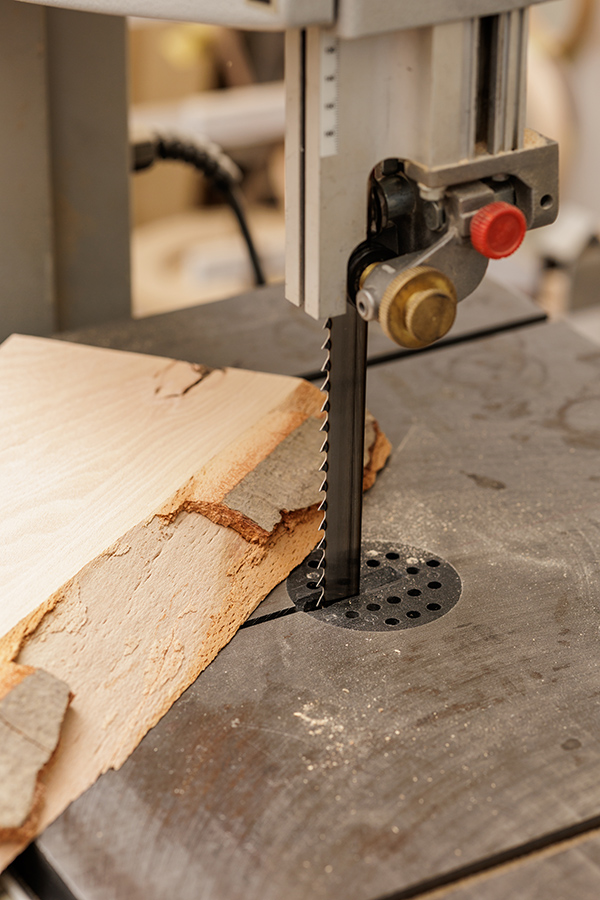 Sierra de cinta vertical que corta tablas de madera en bruto sobre una mesa de trabajo en un taller de carpintería